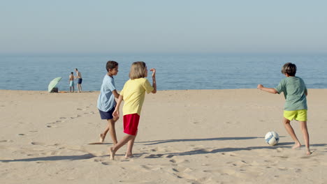 Slow-motion-of-happy-boys-playing-soccer-on-sandy-shore